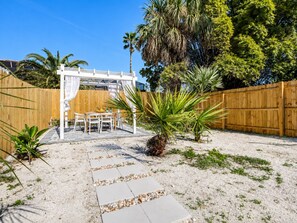A patio area with a pergola, outdoor furniture, and a pathway leading to a wooden fence.