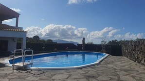 Une piscine avec une terrasse en pierre, un espace couvert et une vue sur les montagnes en arrière-plan.
