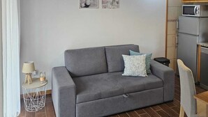 Un salon moderne avec un canapé gris, deux coussins, une petite table d’appoint avec une lampe et un climatiseur fixé au mur.