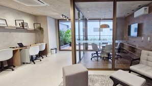 Un espacio de oficina moderno con un separador de vidrio, un televisor montado en la pared y un escritorio con una computadora portátil.