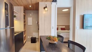 Una cocina compacta con electrodomésticos modernos, un comedor con mesa y sillas, y un dormitorio visible con cama y mesita de noche.