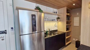 Una cocina moderna con un refrigerador de acero inoxidable, encimeras negras, estantes de madera y un lavamanos integrado.