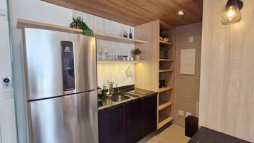 Una cocina moderna con un refrigerador de acero inoxidable, encimeras negras, estantes de madera y un lavamanos integrado.