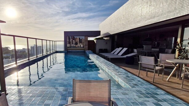 Una piscina infinita en la azotea, con barandilla de cristal, sillones de descanso y zona de bar.