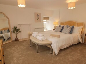 Een slaapkamer met een groot bed, nachtlampjes, een spiegel, een potplant en een open haard.