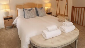 A neatly made bed with checkered pillows, a bedside table with a lamp, a wooden chair, and a small wooden ladder. - Pentwyn (Haverfordwest)