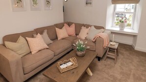 A cozy living room with a brown sofa, a wooden coffee table, and a window with a view of the outdoors. - Pentwyn (Haverfordwest)