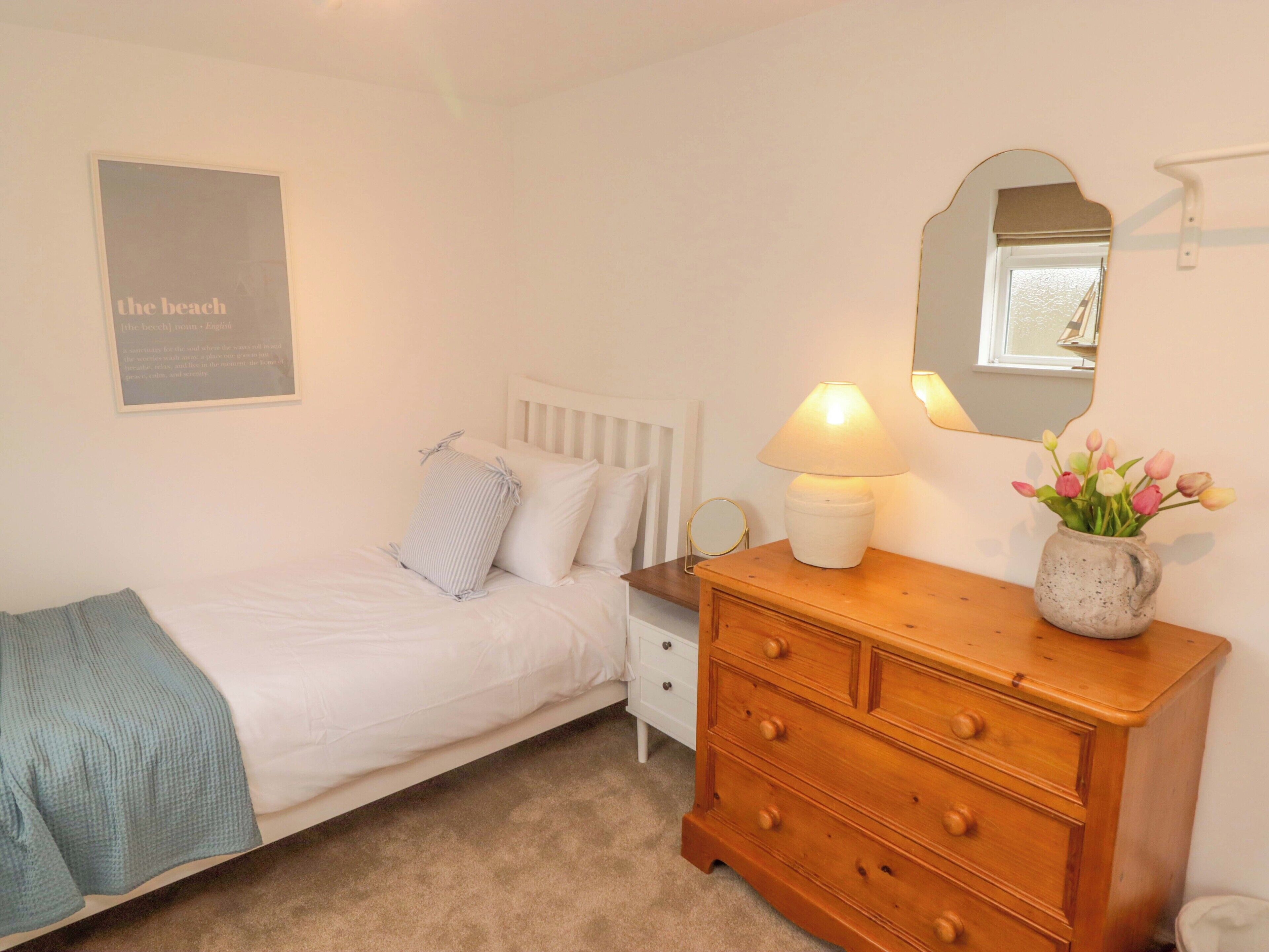 A bedroom with a bed, a dresser, a bedside lamp, a mirror, and a poster on the wall.