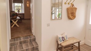 A hallway with a wooden bench, a woven basket, a mirror, and a door leading to a room with a table and chairs. - Pentwyn (Haverfordwest)