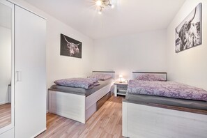 Quarto com duas camas, um guarda-roupa e duas imagens penduradas na parede.