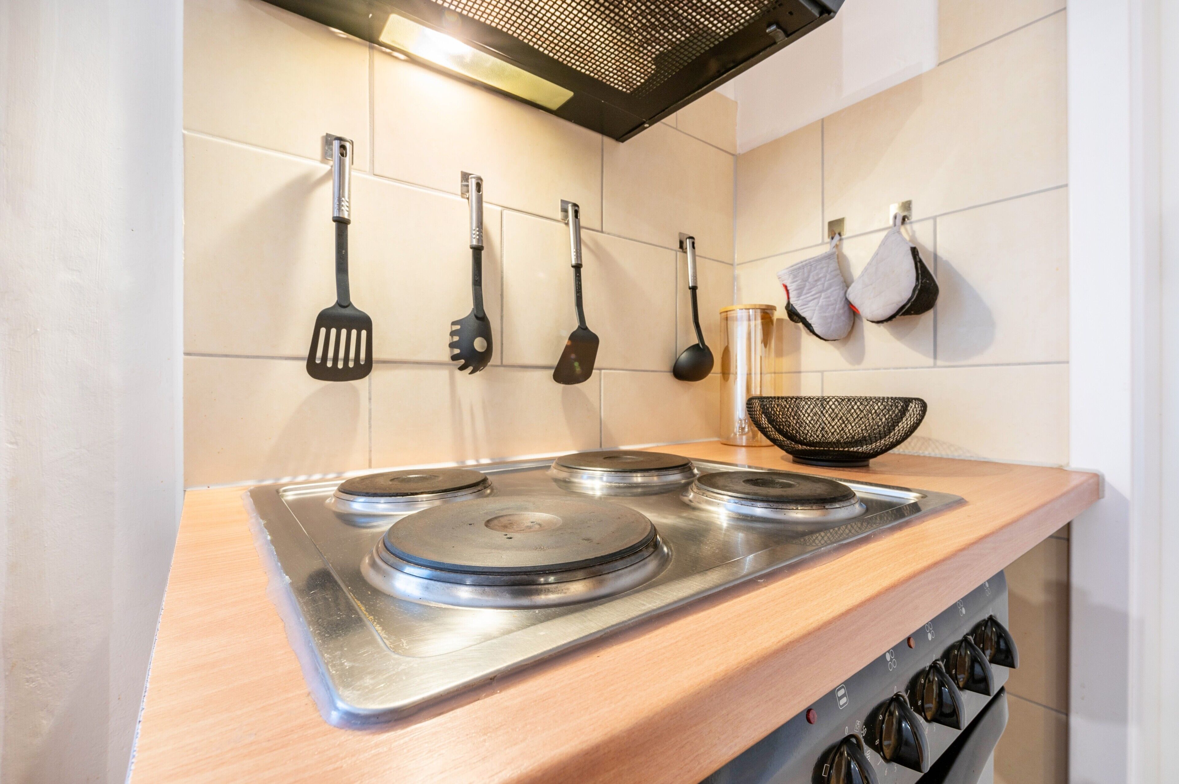 Une cuisine équipée d’une cuisinière en acier inoxydable, d’ustensiles de cuisine suspendus et d’un plan de travail en bois.