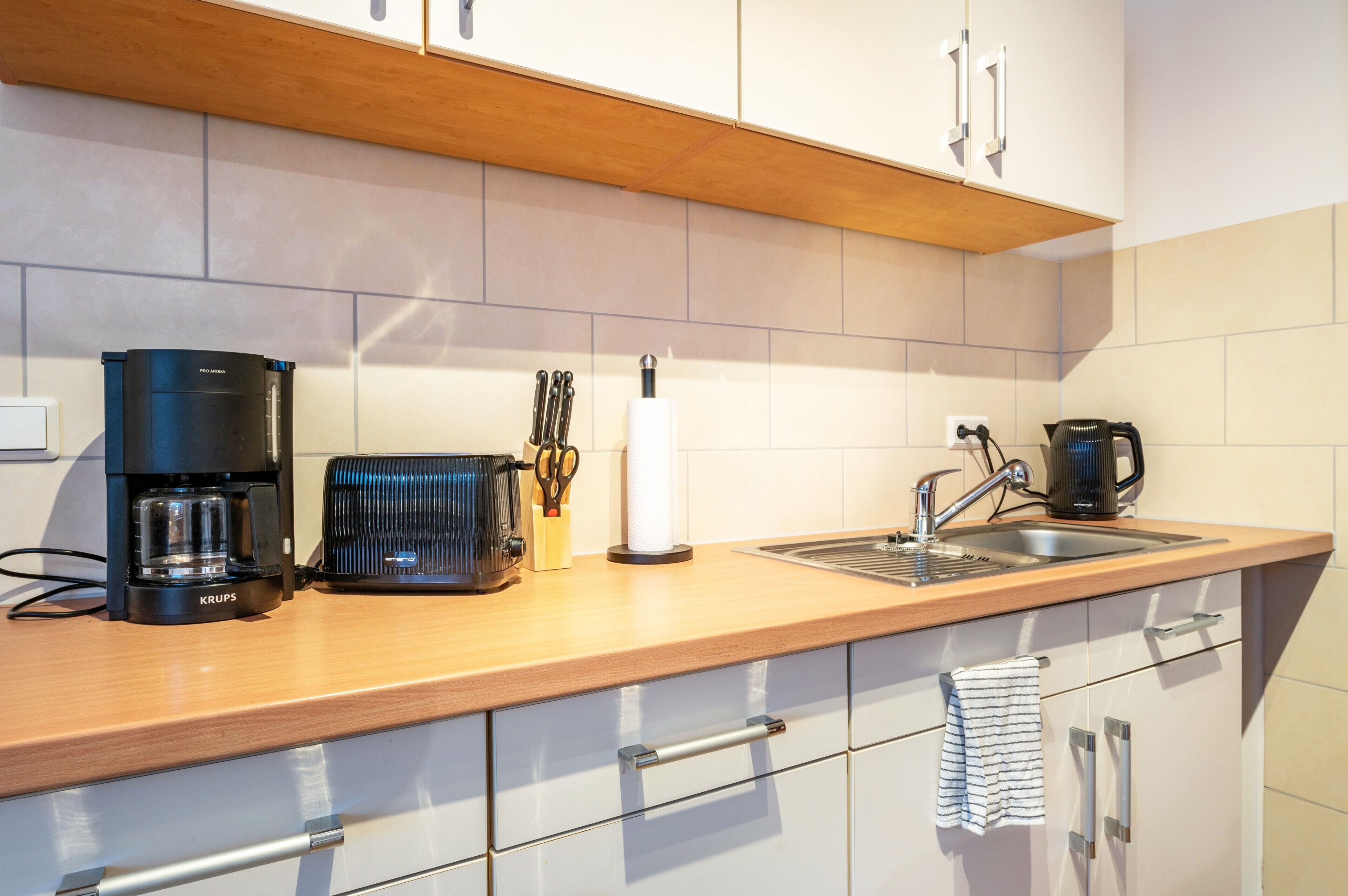 A modern kitchen with a coffee maker, toaster, and kettle on the counter, a sink, and white cabinets.
