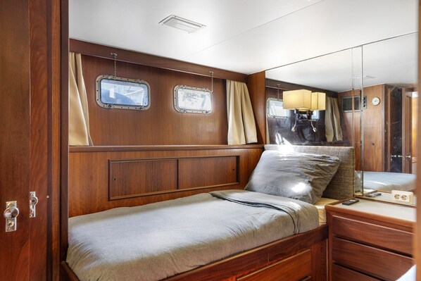 Een compacte, goed verlichte hut met een enkel bed, een dressoir, een spiegel en twee ramen met nummers.