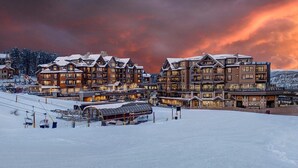 Un lodge de varios pisos con un telesilla al frente, rodeado de terreno cubierto de nieve.