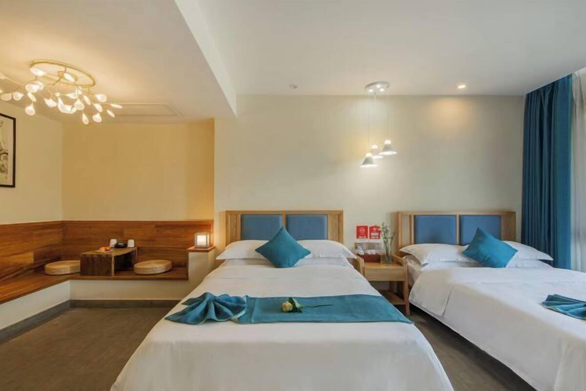 A hotel room with two beds, wooden headboards, a small table with a lamp, and a wall-mounted light fixture.