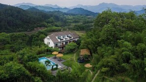 A house surrounded by lush greenery and mountains. - Anji Double Fish Hall Hot Spring Resort B&B (Longwangshan Canyon Drift Shop) (Anji)