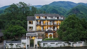 A traditional multi-story building with a courtyard, surrounded by lush greenery and mountains. - Anji Double Fish Hall Hot Spring Resort B&B (Longwangshan Canyon Drift Shop) (Anji)