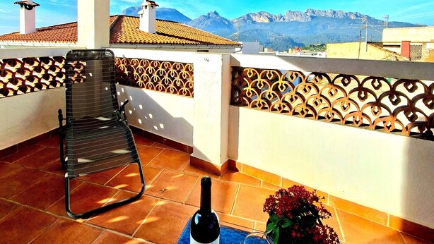 A terrace with a table set for two, a bottle of wine, and a potted plant.