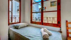 A room with a bed, a window with a view of balconies, and a wooden chair.