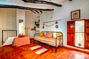 Un dormitorio con cama, puerta de madera, ventana con vista y estante montado en la pared.