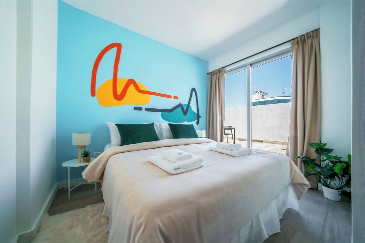 A hotel room with a large bed, a small bedside table with a lamp, a window with curtains, and a view of the outside.