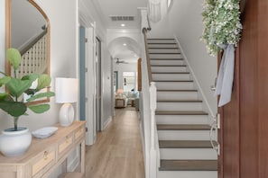 A hallway with a wooden console table, a potted plant, a mirror, and a staircase with a white railing.