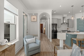 A modern kitchen with a central island, a dining area with a light blue sofa, and a hallway leading to another room.