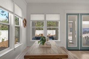 A room with large windows, a wooden table with a tray, and a view of the backyard. - Trae Bien – Private Pool / Pet Friendly / Golf Cart (Santa Rosa Beach)