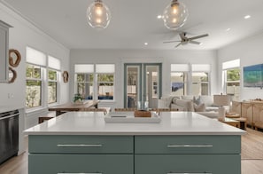 A modern kitchen with a large island, pendant lighting, and a ceiling fan.