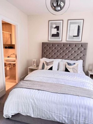 Une chambre à coucher avec une tête de lit capitonnée, du linge de lit blanc et deux œuvres d’art encadrées accrochées au mur.