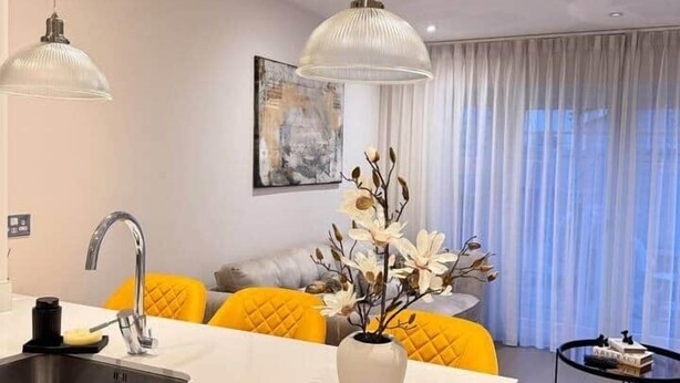 Une cuisine moderne dotée d’un  îlot central, d’un évier et d’un coin repas avec des chaises jaunes. Un vase rempli de fleurs est posé sur l’îlot.