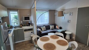 Une cuisine compacte équipée d’un four à micro-ondes, d’un évier et d’une cuisinière. On y trouve également un coin repas avec une table ronde et des chaises. Un canapé et une petite table ronde sont également visibles.