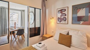 Habitación de hotel con cama, escritorio y vista de la ciudad a través de amplias ventanas.