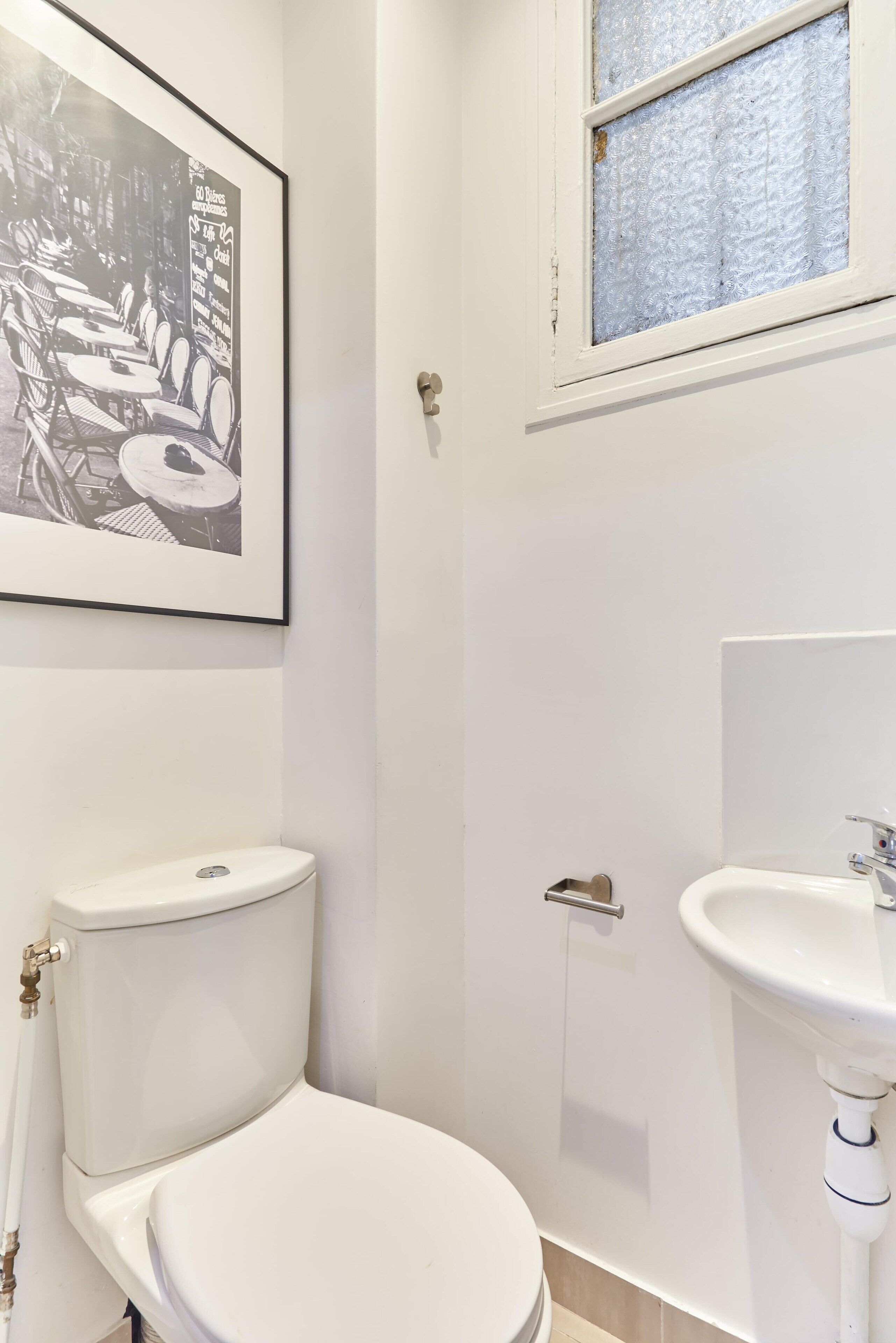 A small, white bathroom with a toilet, sink, and a framed picture on the wall.