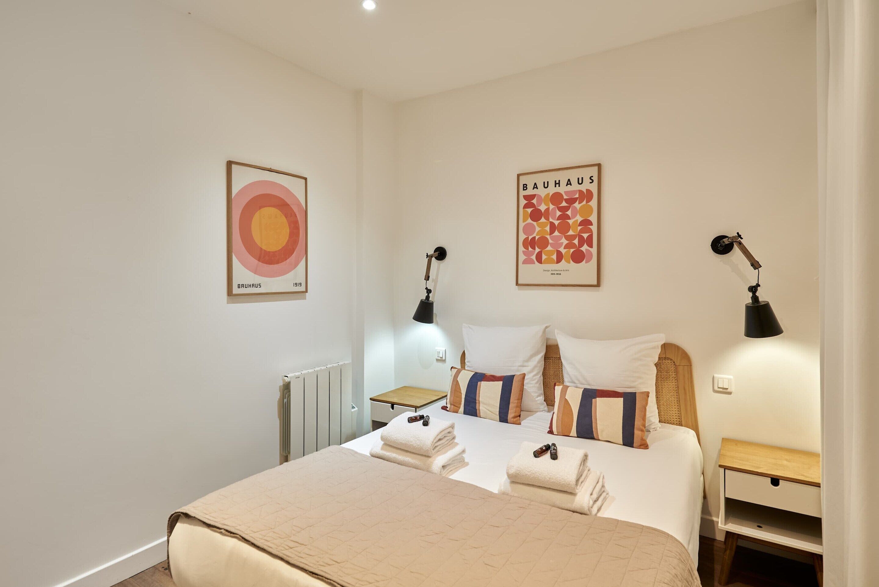 A bedroom with a bed, two bedside tables, a radiator, and two wall-mounted lamps.