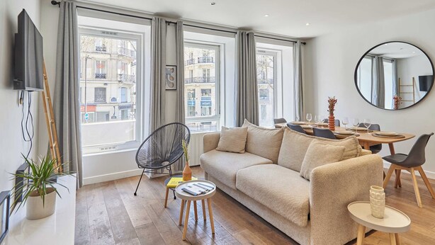 Una sala de estar moderna con un sofá, una mesa de comedor, sillas, un televisor y ventanas amplias.