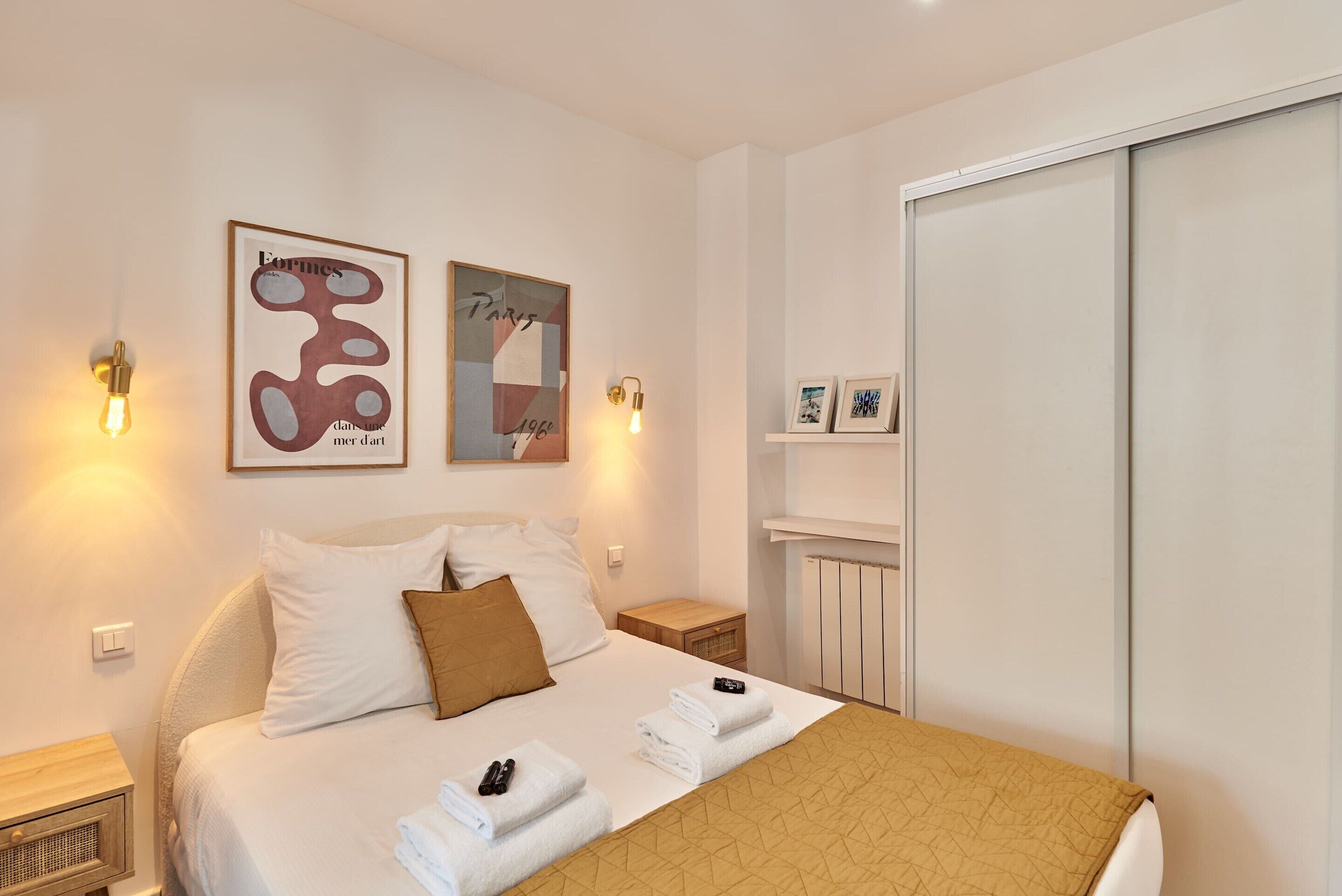 Une chambre d’hôtel bien aménagée, avec un lit, des tables de chevet, des œuvres d’art accrochées au mur et une armoire.
