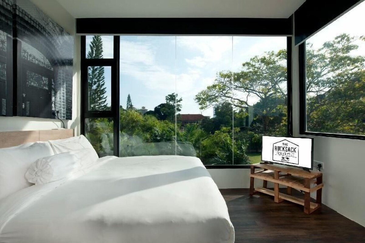 Une chambre moderne avec un grand lit, une vue sur l’extérieur et un panneau posé sur une petite table.
