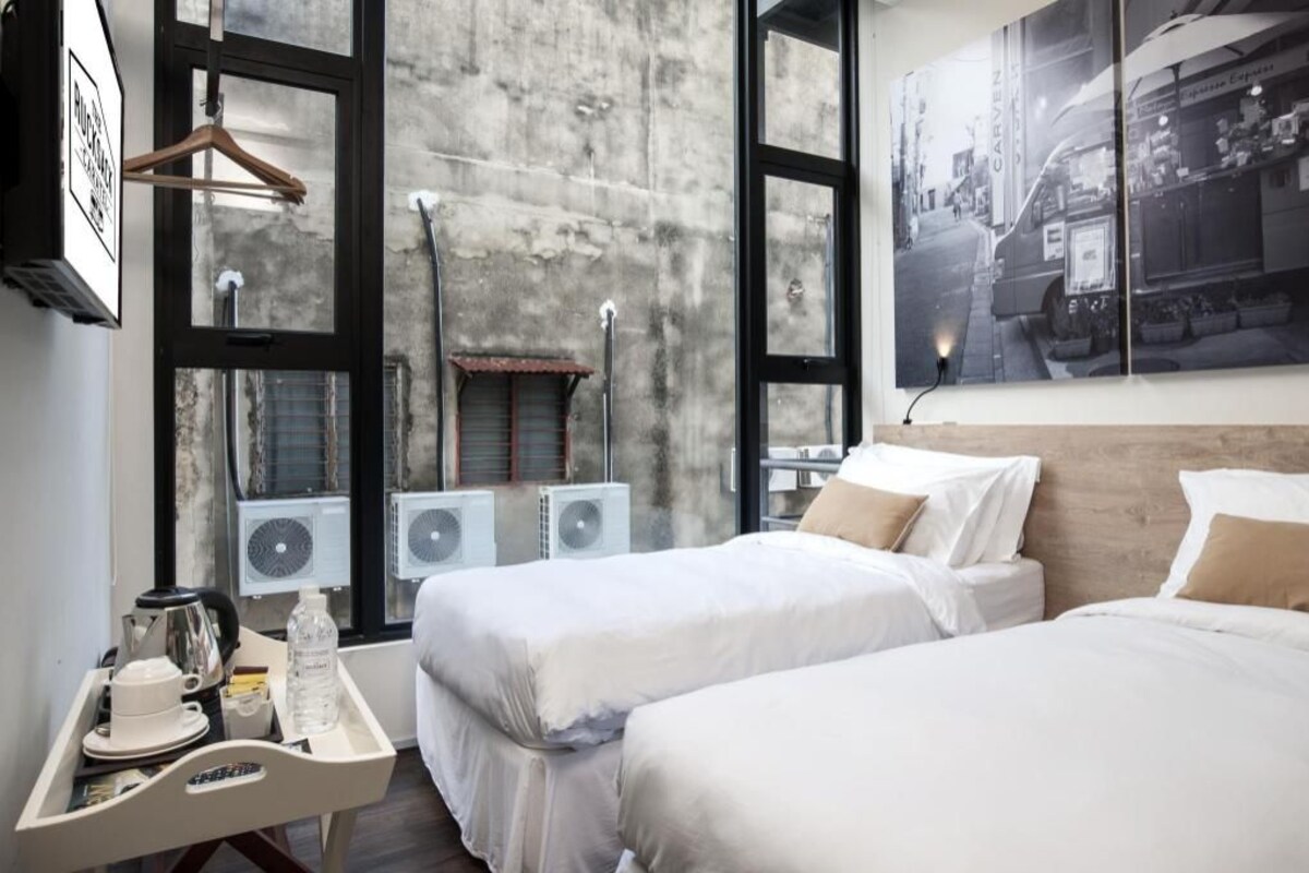 A hotel room with two beds, a window with a view of the street, and a small table with a kettle and a bottle.