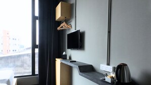 A modern hotel room with a large window, a flat-screen TV mounted on the wall, a built-in kitchen counter with a kettle, and a bedside table. - Rucksack Inn Premium Melaka (Malacca City)
