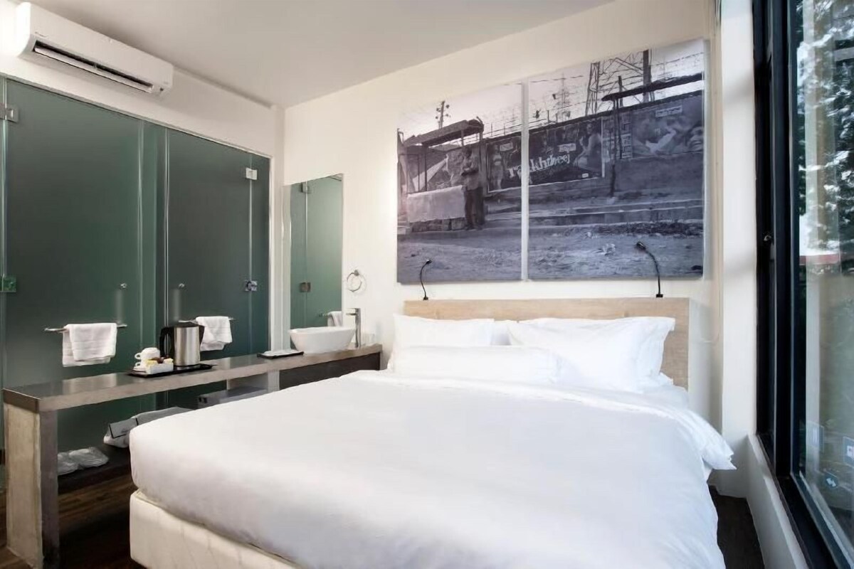 A hotel room with a bed, a vanity with a mirror, and a large window.