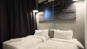 A hotel room with two beds, dark curtains, a wall-mounted light, and a poster. - Rucksack Inn Premium Melaka (Malacca City)