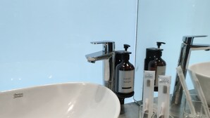 A bathroom with a white sink, a mirror, and toiletries including hand wash and toothbrushes. - Rucksack Inn Premium Melaka (Malacca City)