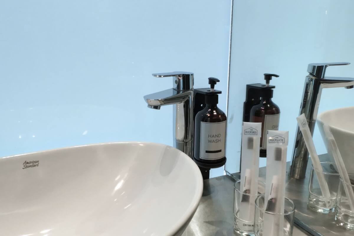 Ein Badezimmer mit Waschbecken, Spiegel und Toilettenartikeln, darunter Handseife und Zahnbürsten.