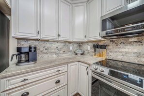 A kitchen with white cabinets, a built-in microwave, a coffee maker, and a knife block.