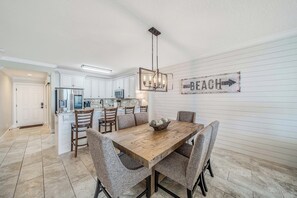 A modern kitchen with white cabinets, stainless steel appliances, and a dining area with a wooden table and patterned chairs. - NEW Emerald Isle 2009 "The Shore Break" Pool, FREE Perks&Beach Service for 4! (Panama City Beach)