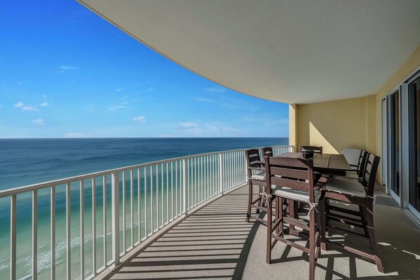 A balcony with a view of the ocean, a table with chairs, and a railing.