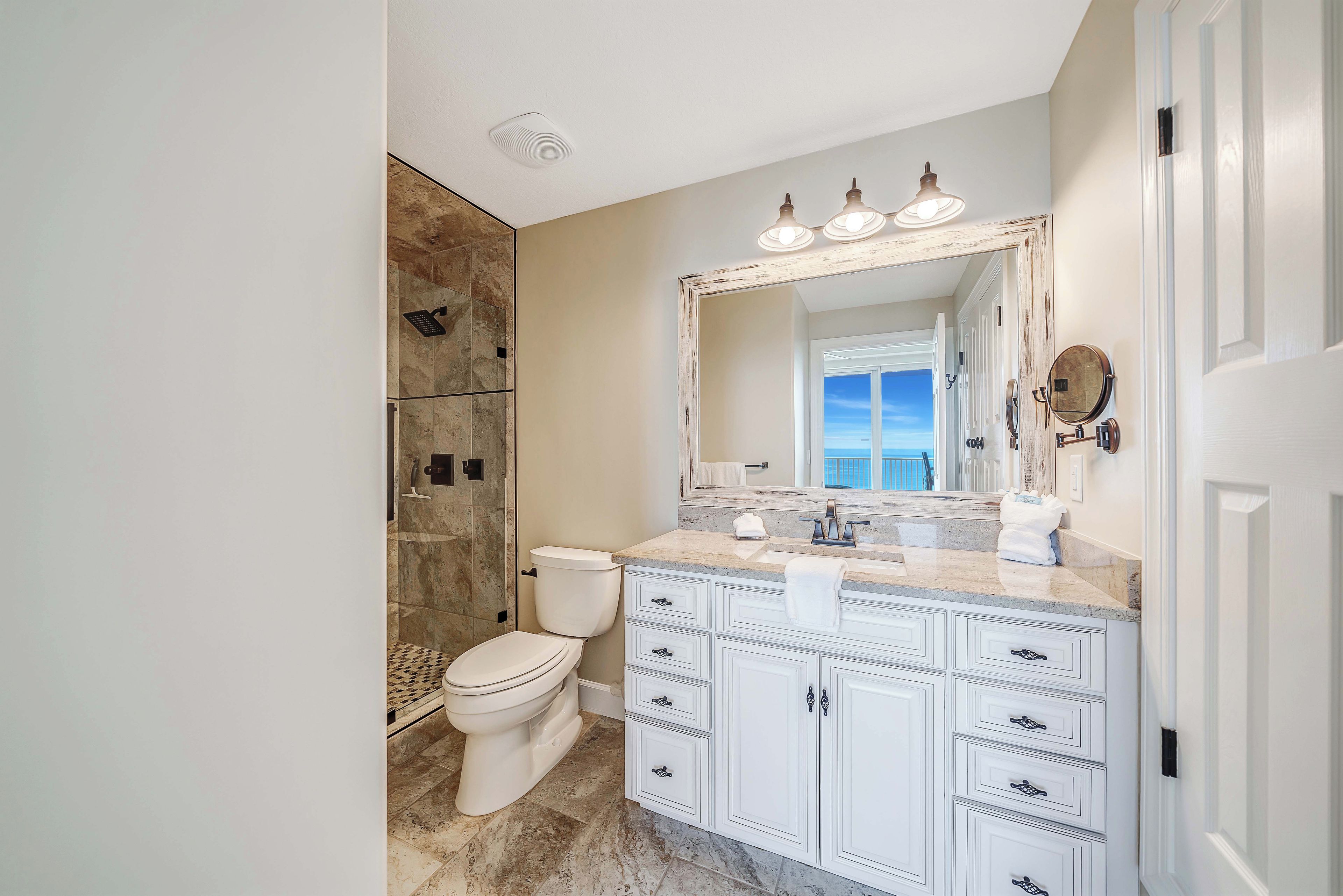 A bathroom with a white toilet, a shower, and a vanity with a mirror.