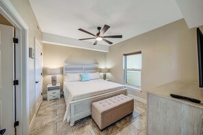A bedroom with a bed, bedside tables, a ceiling fan, a window, and a TV.