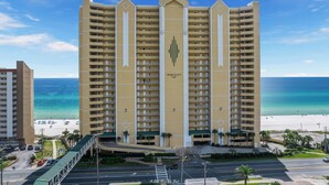 Un hôtel de grande hauteur avec une entrée centrale, de nombreux balcons et une vue sur la plage.